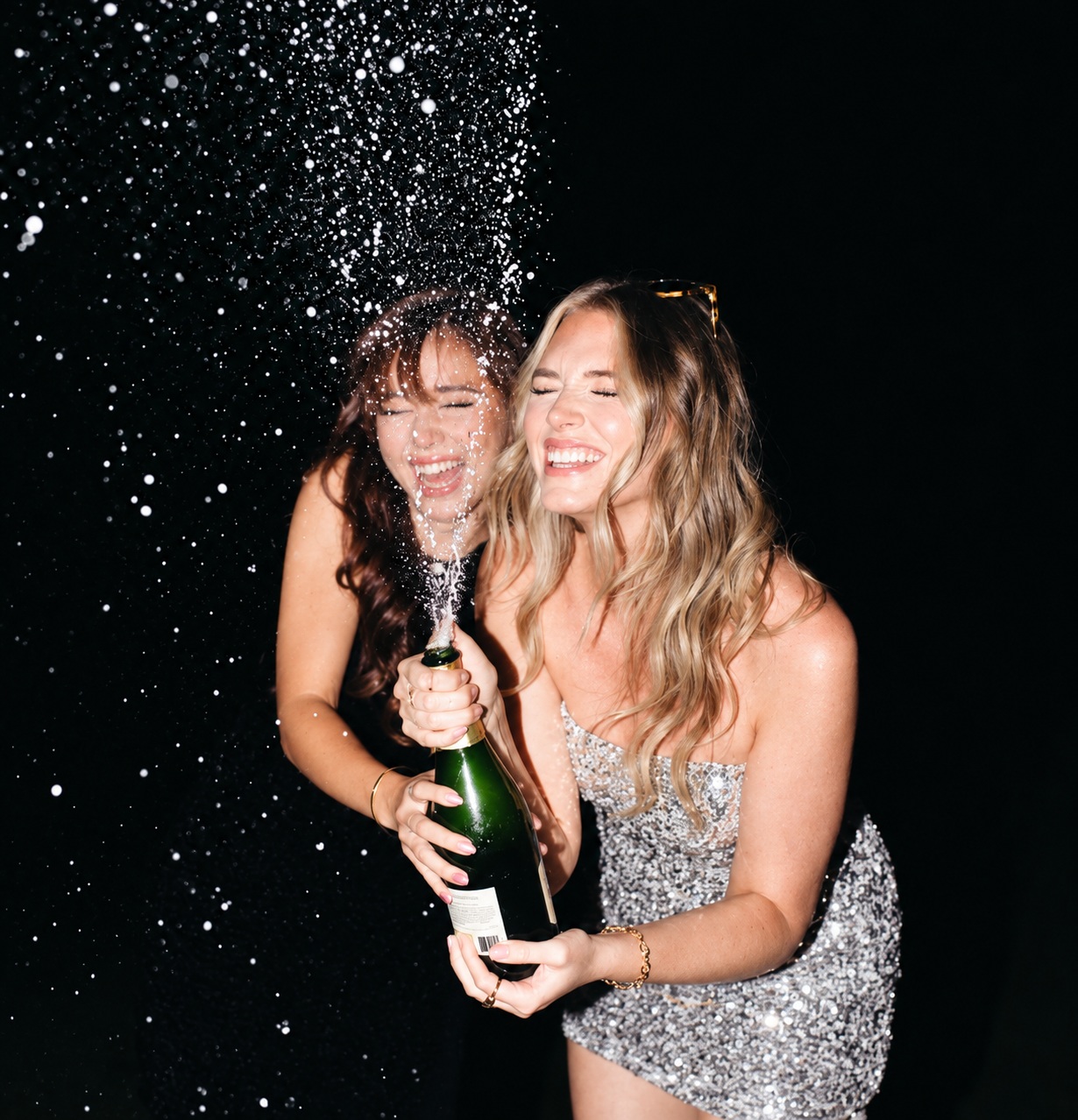 Two friends laughing as a bottle sprays against a black background