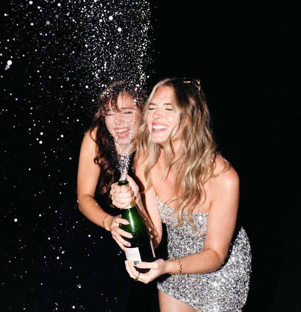 Two friends laughing as a champagne bottle sprays