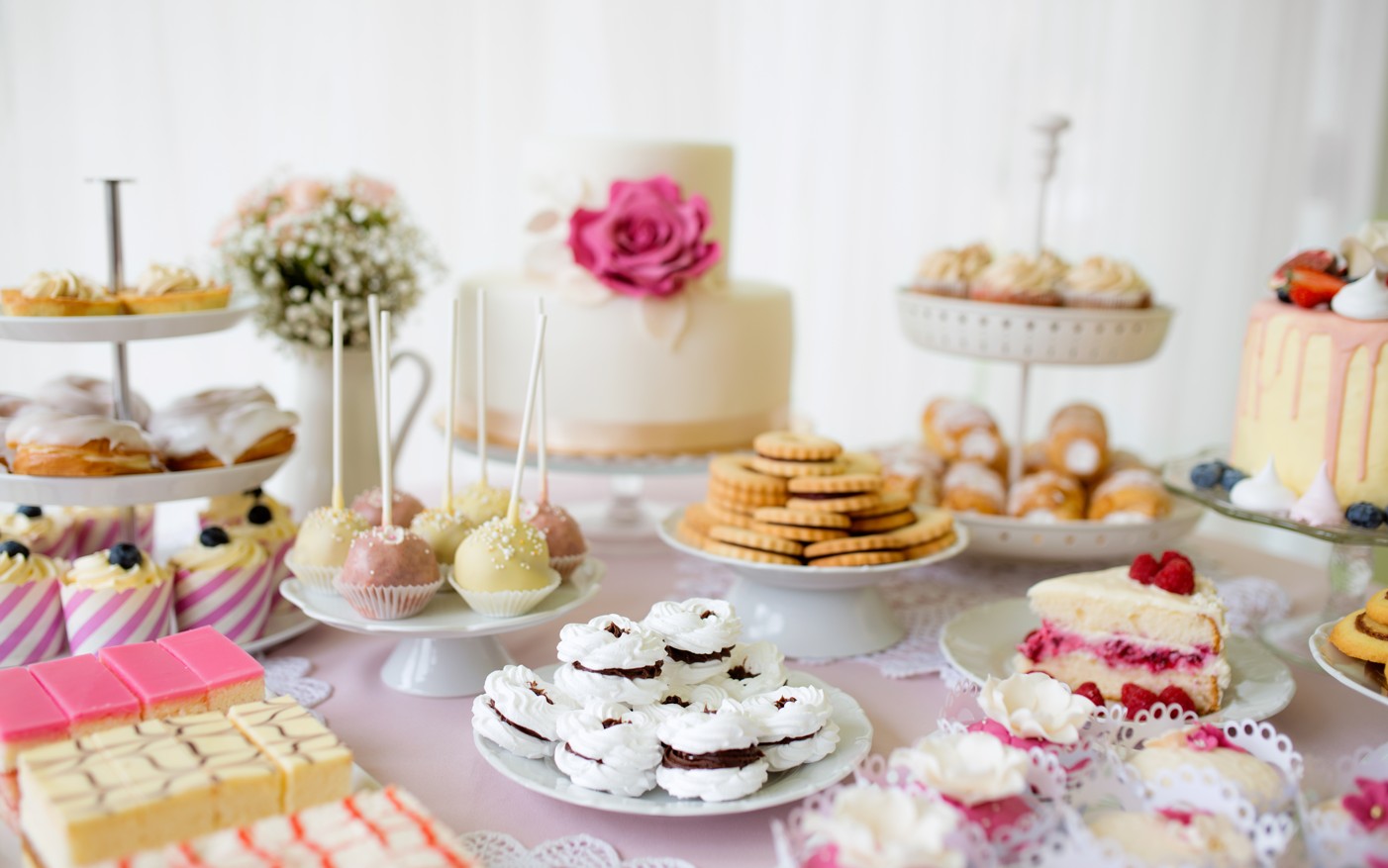 A high tea table of cakes, cake pops, macarons, scones and a two-tier cake with a pink rose
