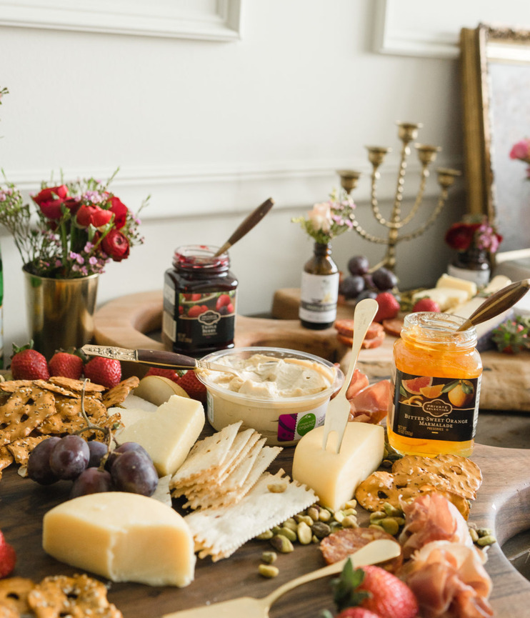 A grazing table of cheeses, crackers, jams, prosciutto, strawberries and grapes by a candelabra