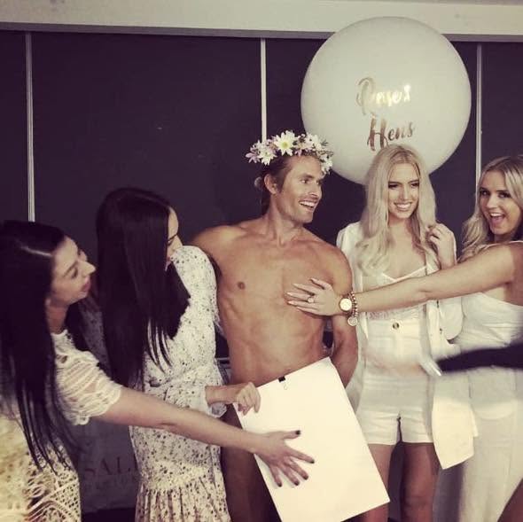 Hens laughing with the shirtless model, who holds a drawing board in front of him