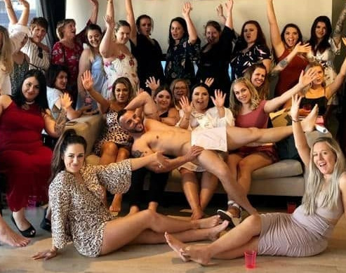 A big hens group cheering with their arms up in the gallery photo, the model lying across their laps behind a sheet of paper