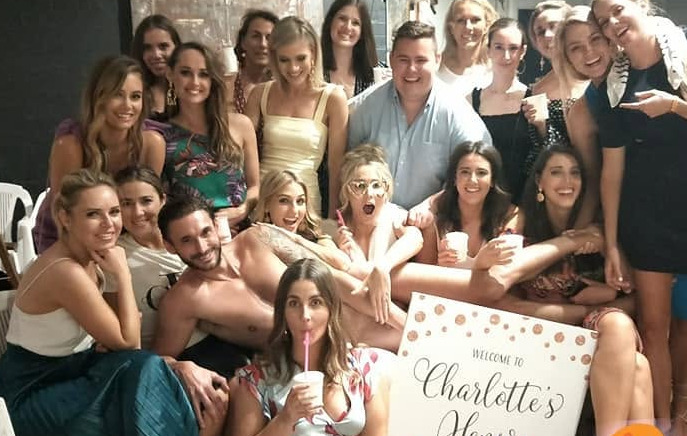 A hens group in a lounge room with a welcome sign for the bride's hens and the model lying across laps