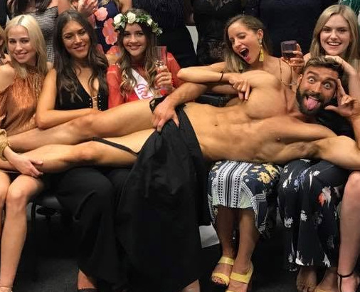 The bride in a flower crown and sash with the model pulling a face across the group's laps
