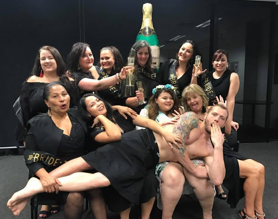 Hens in black with bride sashes and glasses of bubbles, the model lying across their laps