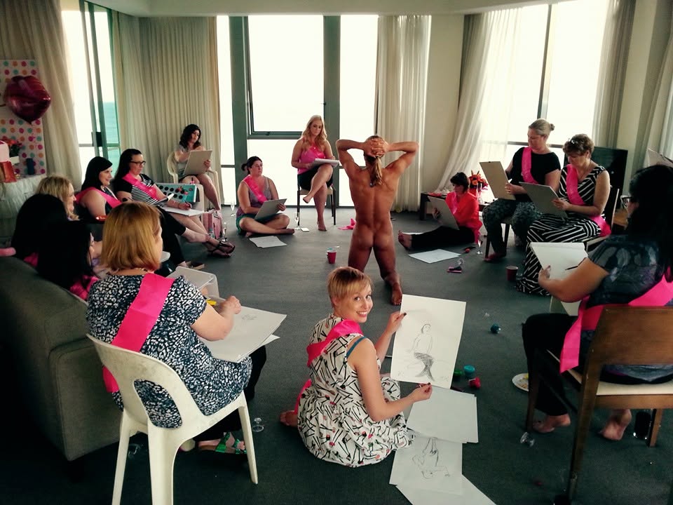 Hens in pink sashes sketching in a circle around the model in a high-rise apartment lounge