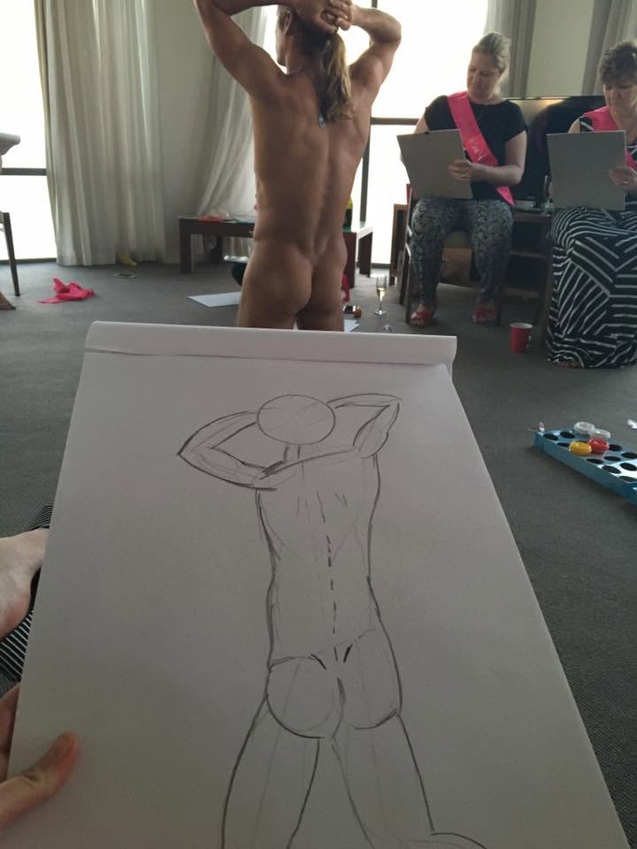 A sketch pad in the foreground with a pencil drawing of the model, who poses with his back to the room while hens in pink sashes draw