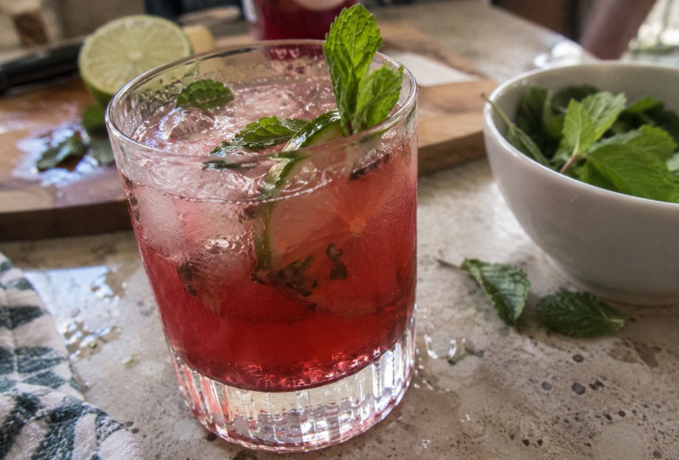 A pomegranate and lime drink with fresh mint in a tumbler, a bowl of mint beside it