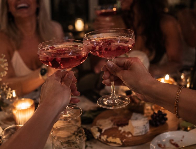 Two coupes of pink bubbles with pomegranate seeds clinking over a candlelit table