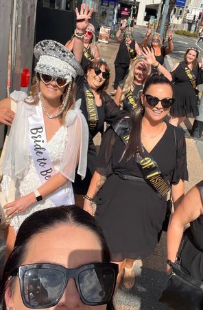 A bride to be in a crown and sash walking out with her hens group