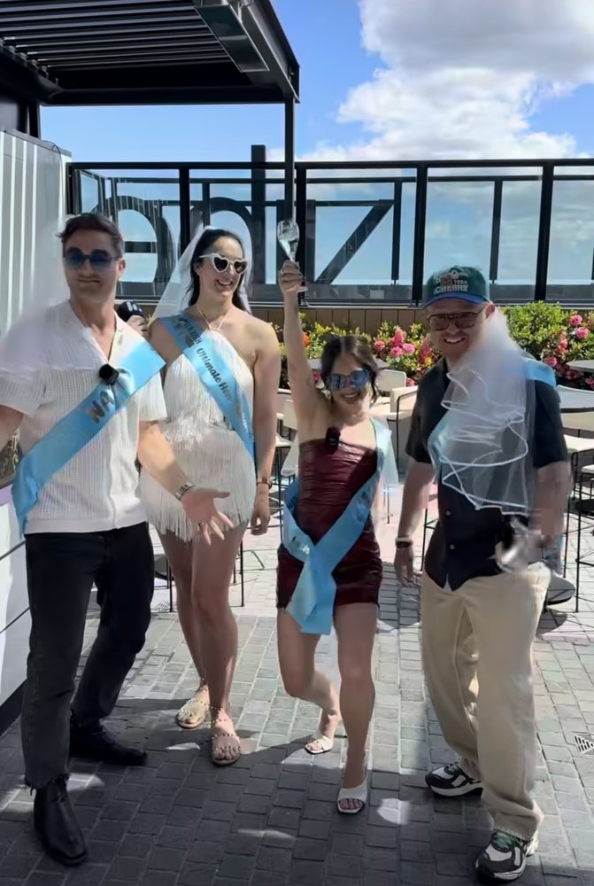 Hens in sashes, with two blokes in veils and sashes, on a Sydney rooftop on the 2Day FM Hen-a-thon day