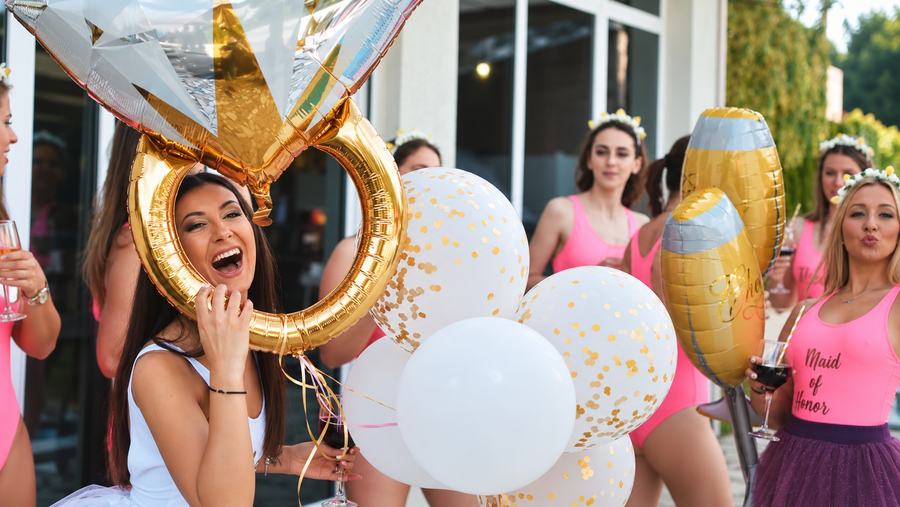 A bride to be laughing behind a giant gold ring balloon