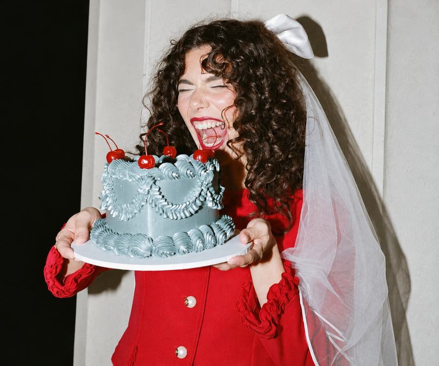 A bride to be in red with a veil holding a decorated cake