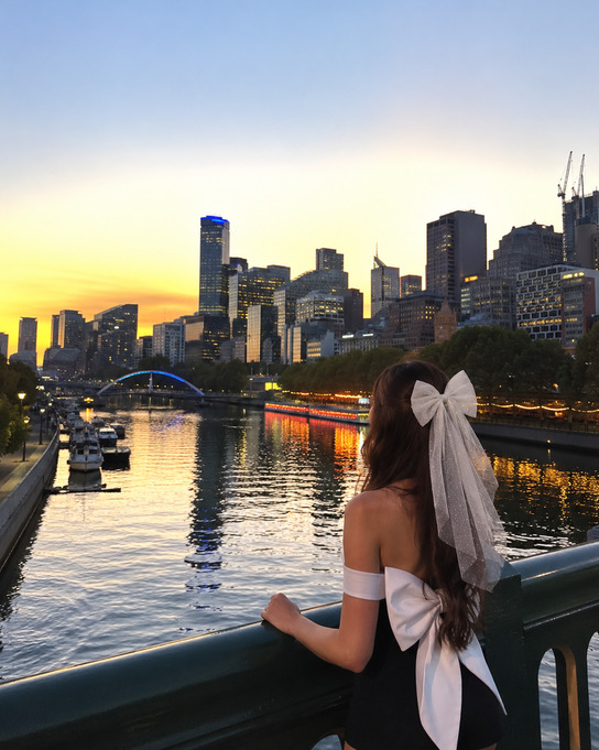A bride to be in a bow veil looking out over the Yarra River to the Melbourne skyline at sunset