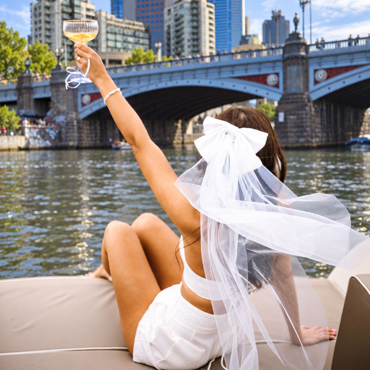 A bride to be in a bow veil raising a coupe of bubbles on a boat on the Yarra River in Melbourne