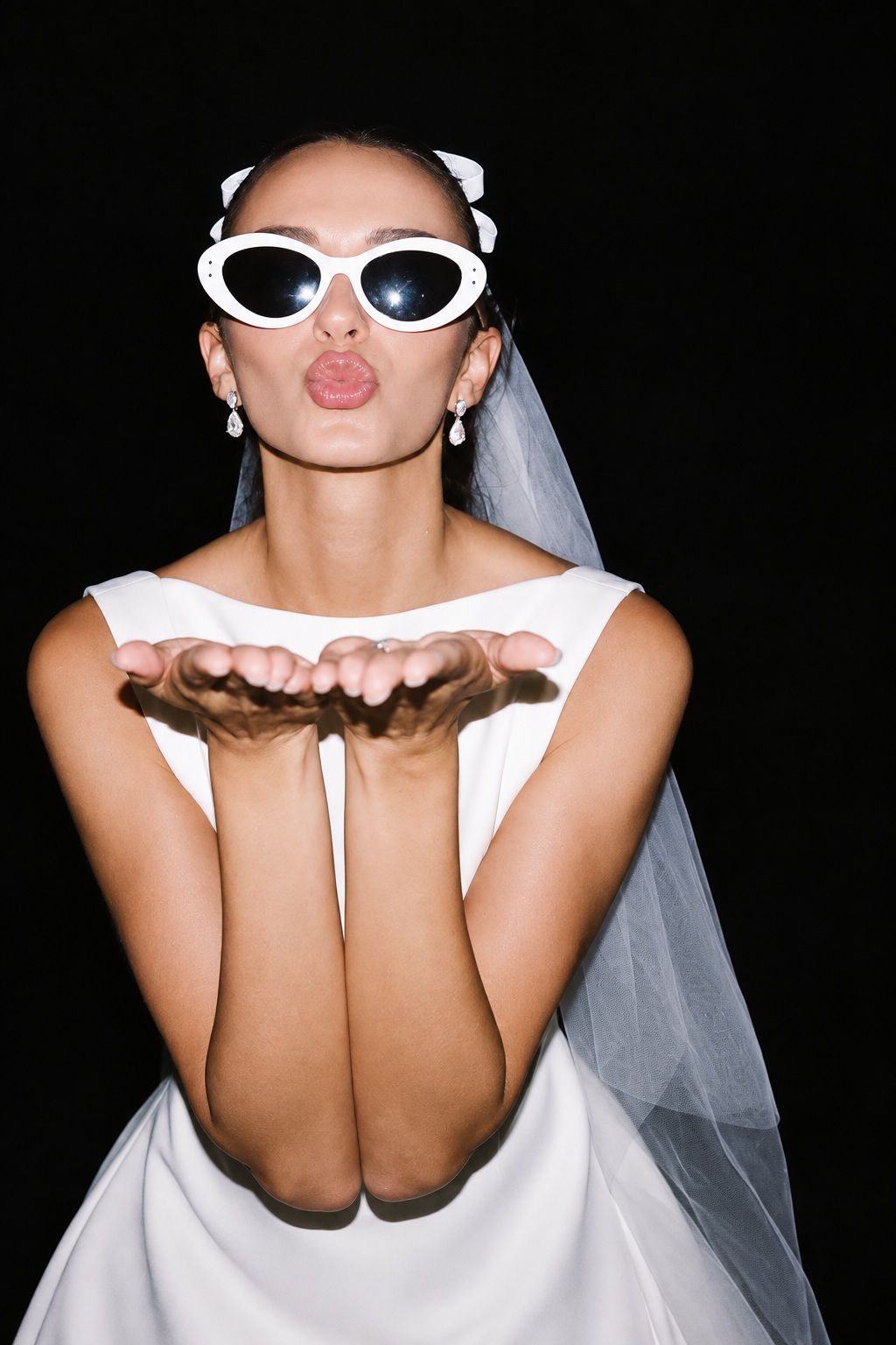 A bride to be in a veil and white sunglasses blowing a kiss