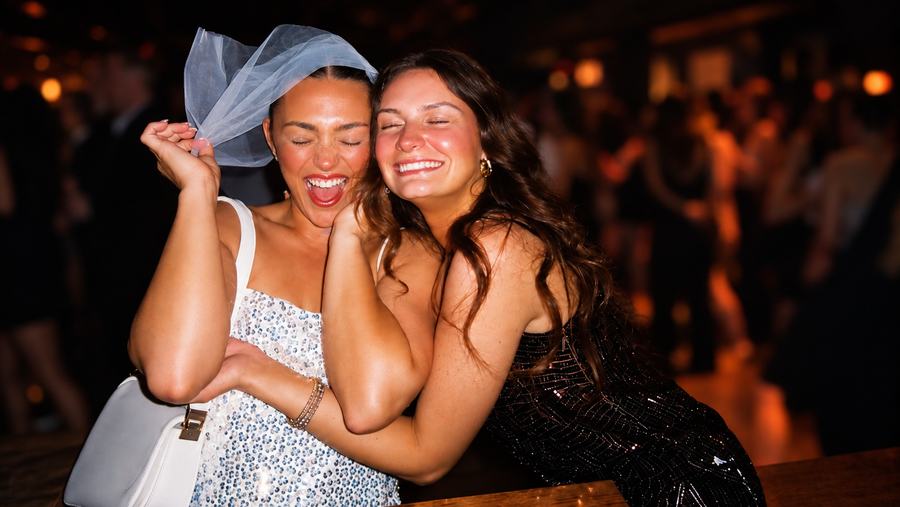 A bride to be in a veil hugging a friend, both laughing