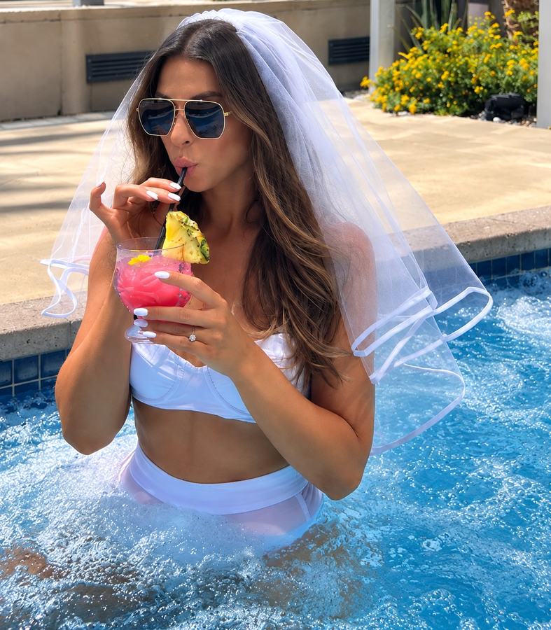 A bride to be in a veil and sunglasses with a frozen cocktail in the pool