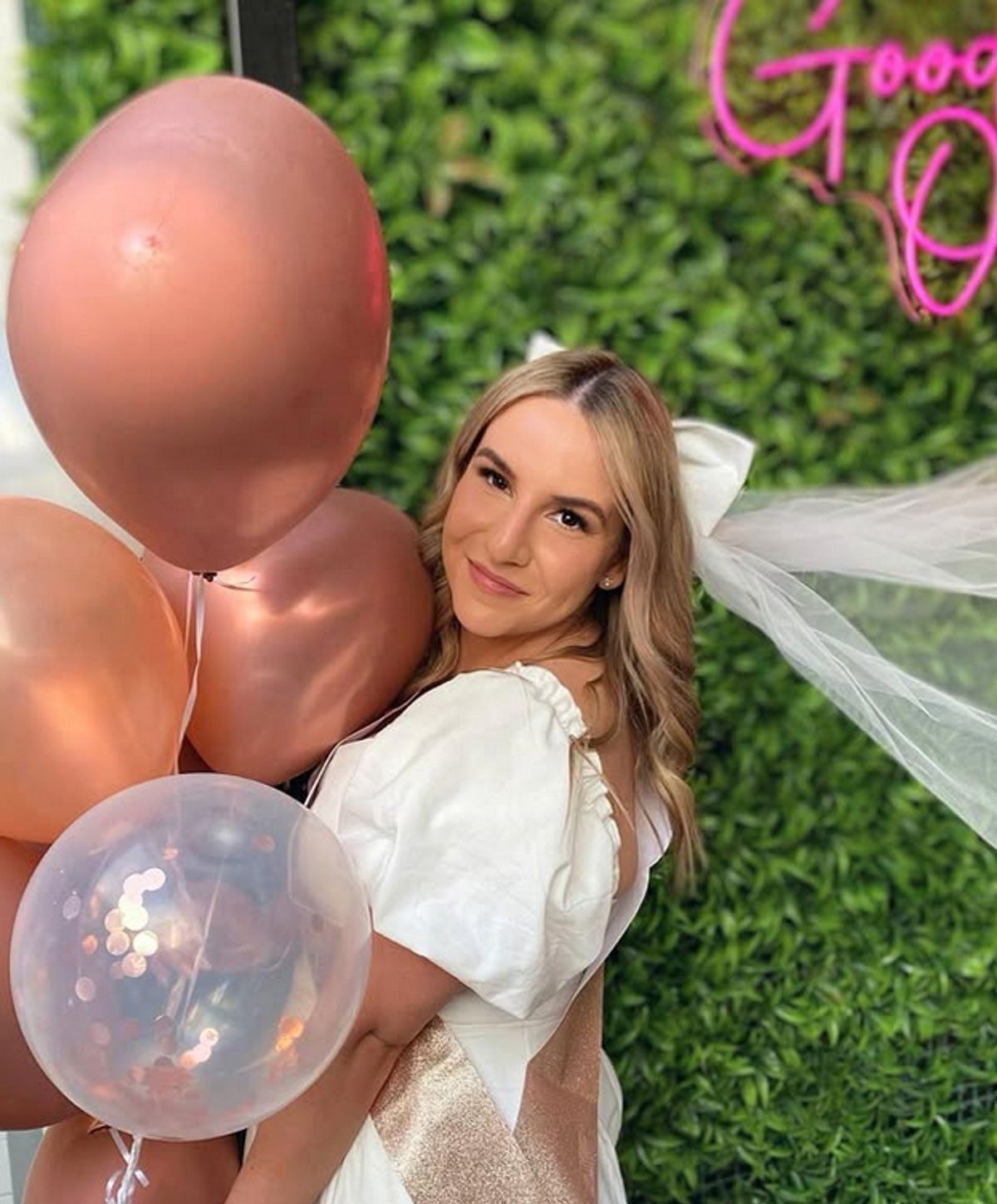 A bride to be in a white dress and veil beside rose-gold balloons