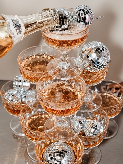 Sparkling wine being poured into a tower of coupe glasses with disco balls
