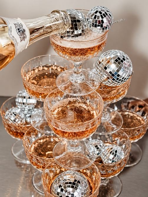 Sparkling wine poured into a tower of coupe glasses with disco balls
