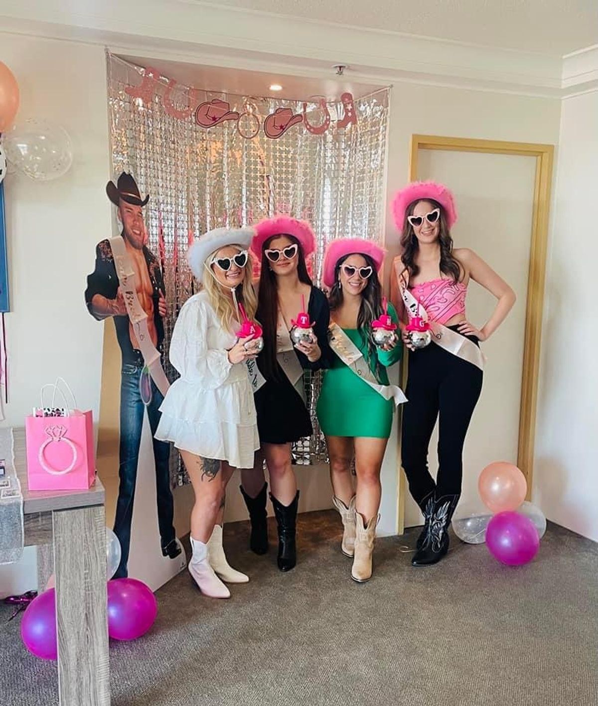 Friends in pink cowgirl hats and sashes in front of a pink tinsel backdrop