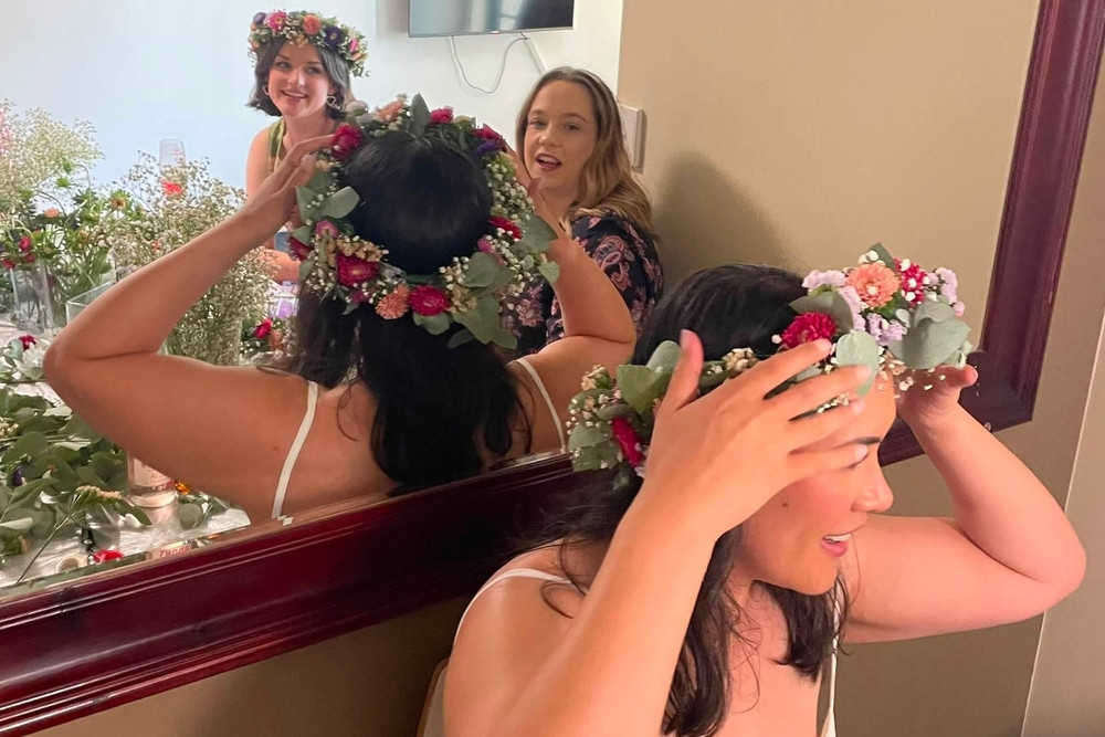 A guest placing her finished fresh flower crown on her head in front of a mirror while her friends look on