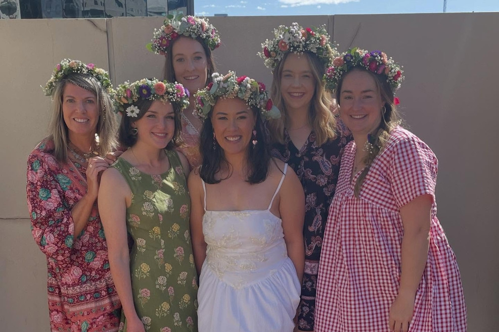 Five friends in fresh flower crowns and summer dresses standing together in the sun, the bride in white in the middle