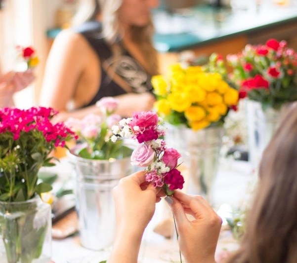 Hands threading pink blooms onto a flower crown