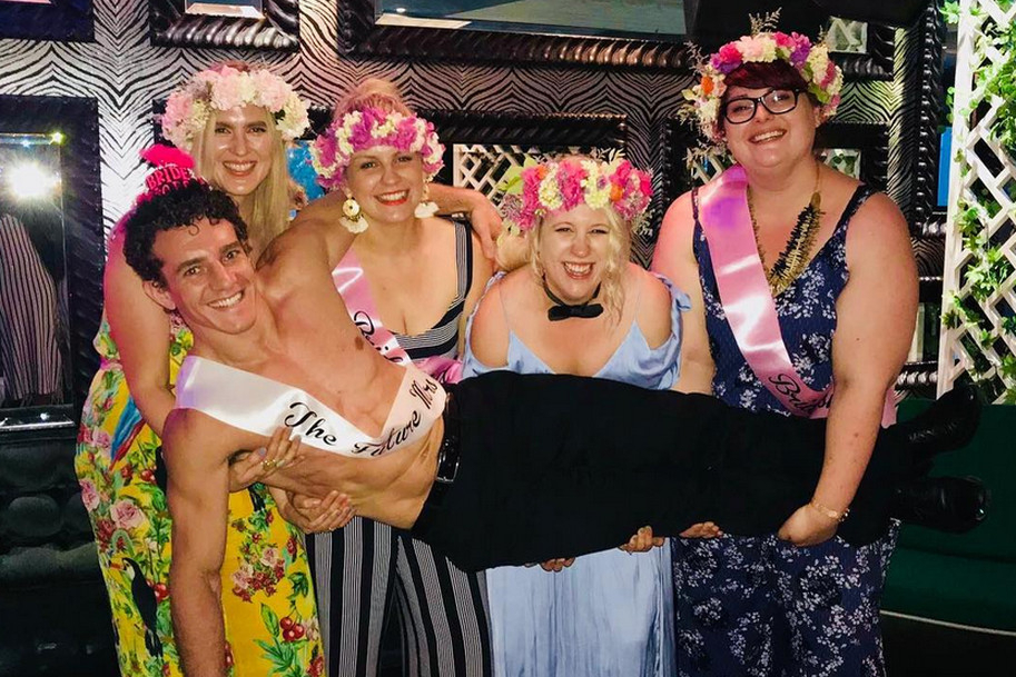 Four friends in flower crowns and sashes laughing as they lift our topless waiter
