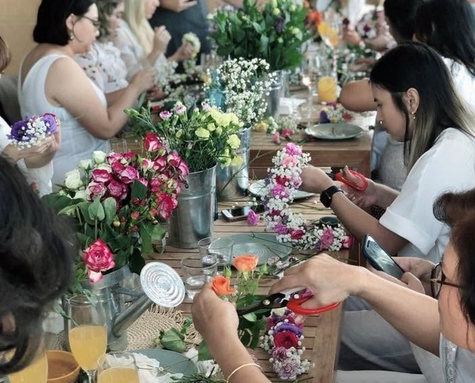 Friends making flower crowns at a long table set with flowers and brunch drinks