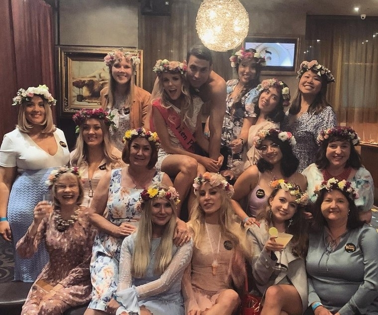 A big hens group in flower crowns with their topless waiter in a lounge at night