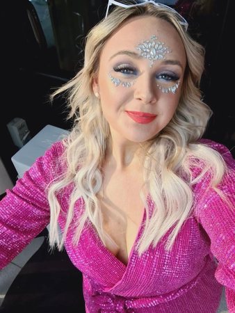 A hen in a hot pink sequin jacket and face gems taking a selfie