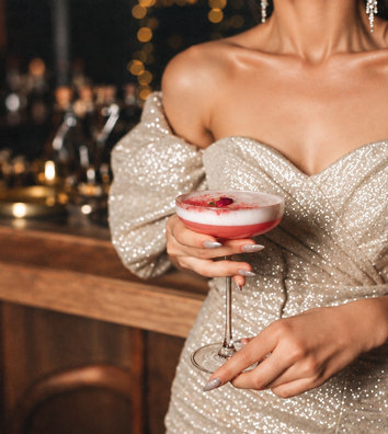 A hen in a gold sequin dress holding a pink cocktail at a candlelit bar