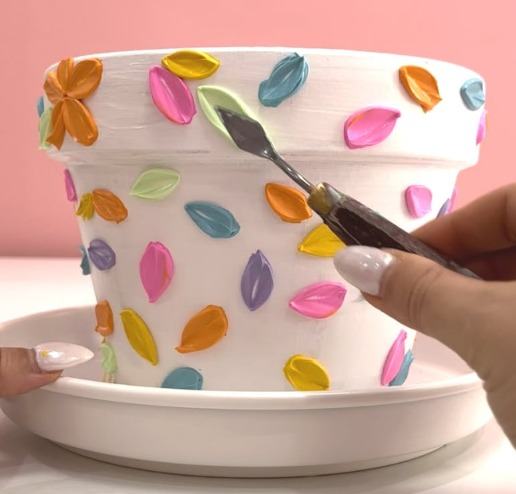 A hand painting petals onto a terracotta pot at a craft session