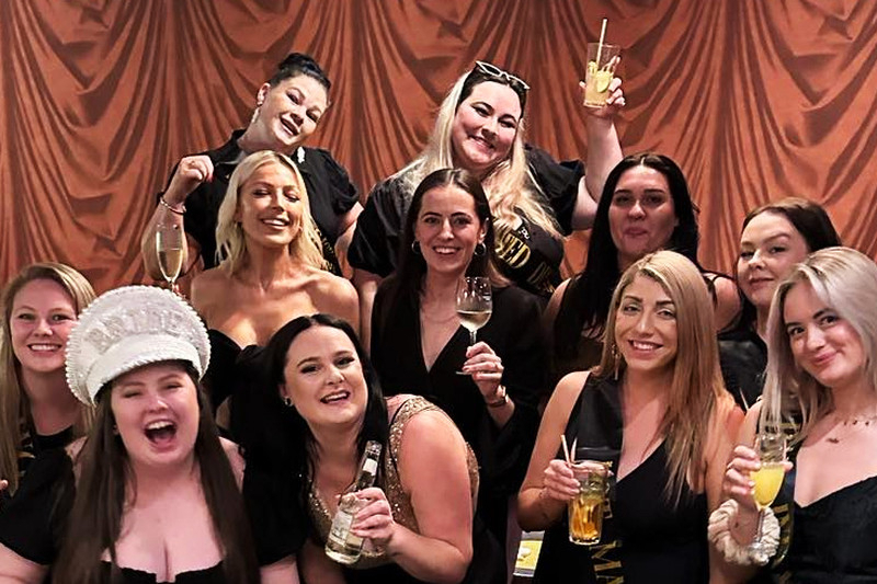 A hens crew dressed up for the night out, laughing together in a red lounge