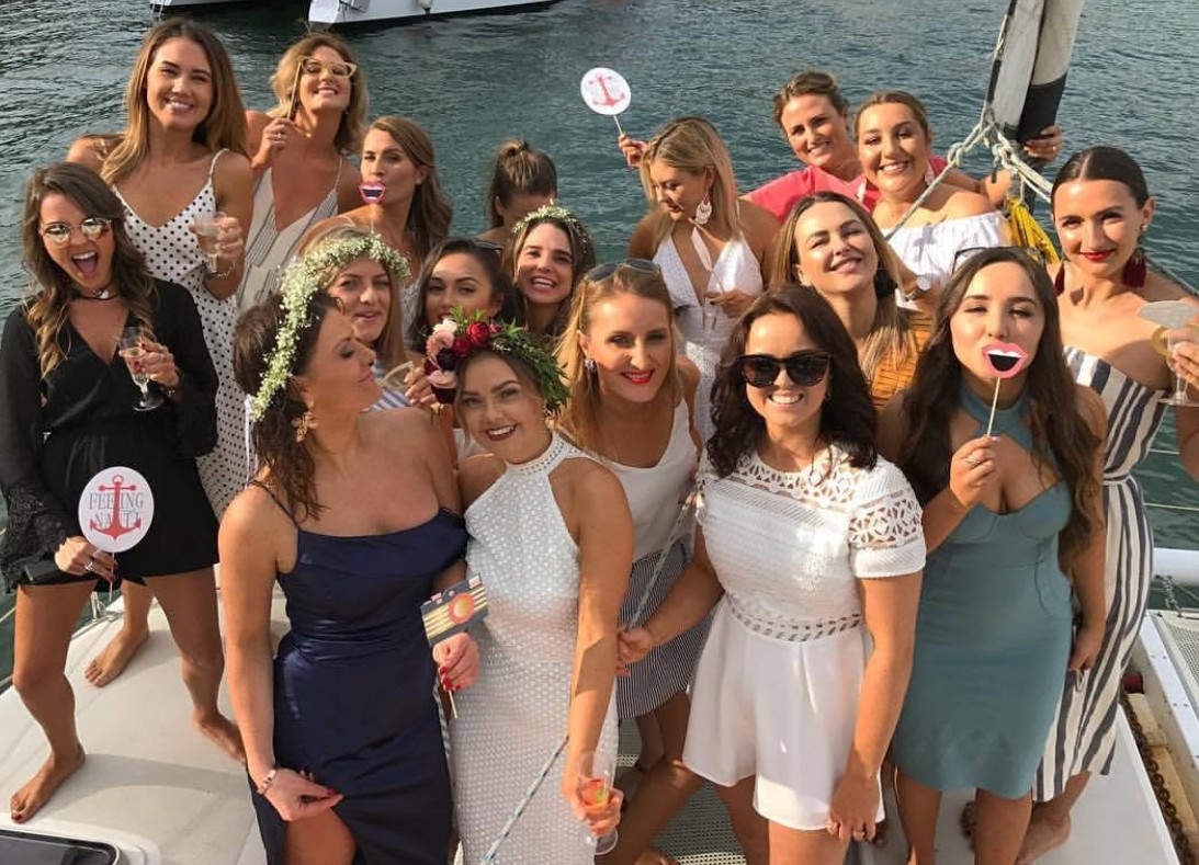 A hens crew with Feeling Nauti photo props and flower crowns on a catamaran