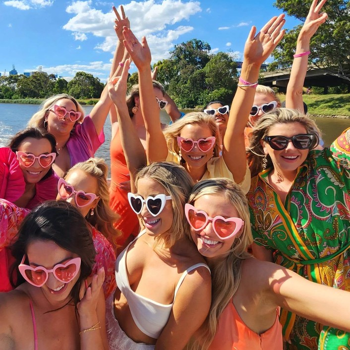 A crew in pink heart sunglasses with their arms in the air on a sunny deck
