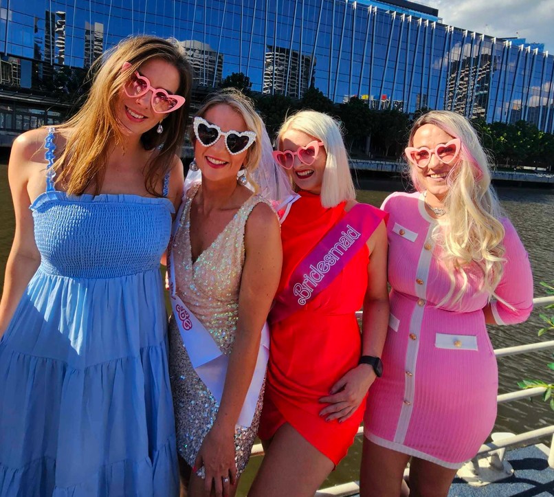 The bride in silver sequins and her veil with her bridesmaids in heart sunglasses, the river behind them