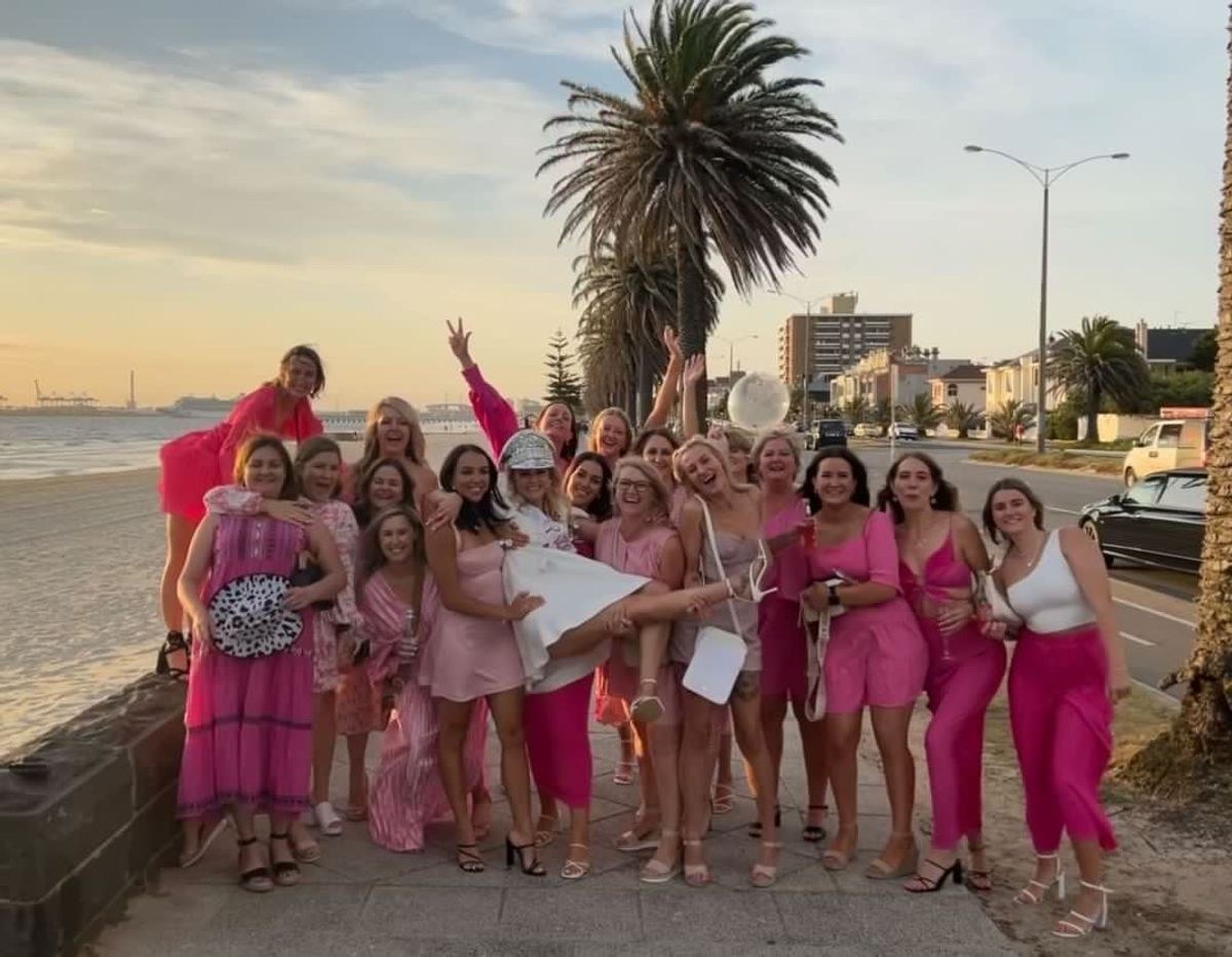 A big hens group celebrating on a beachfront at sunset beside a palm tree