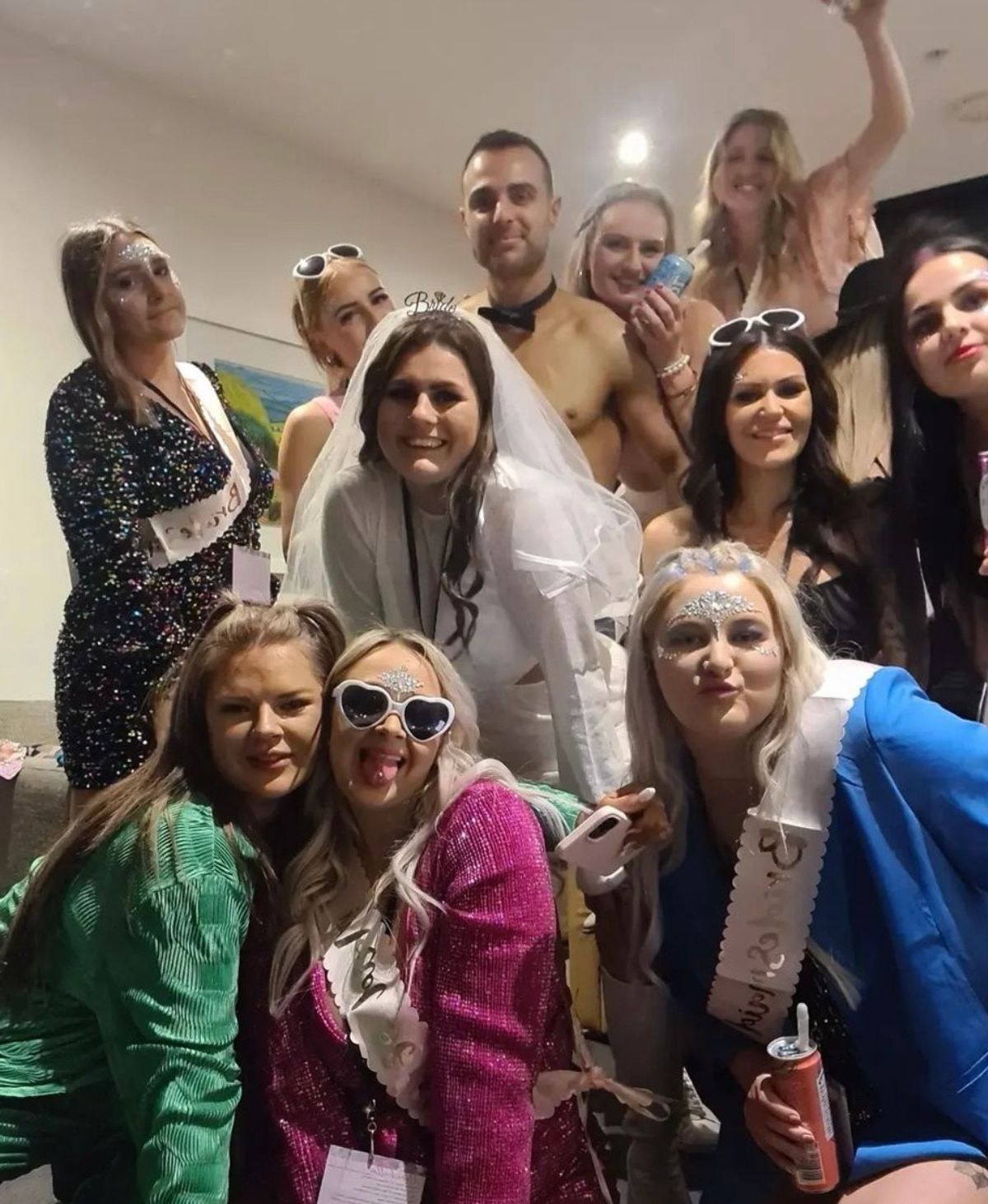 A bride in a veil and heart sunglasses in a hens group selfie at night