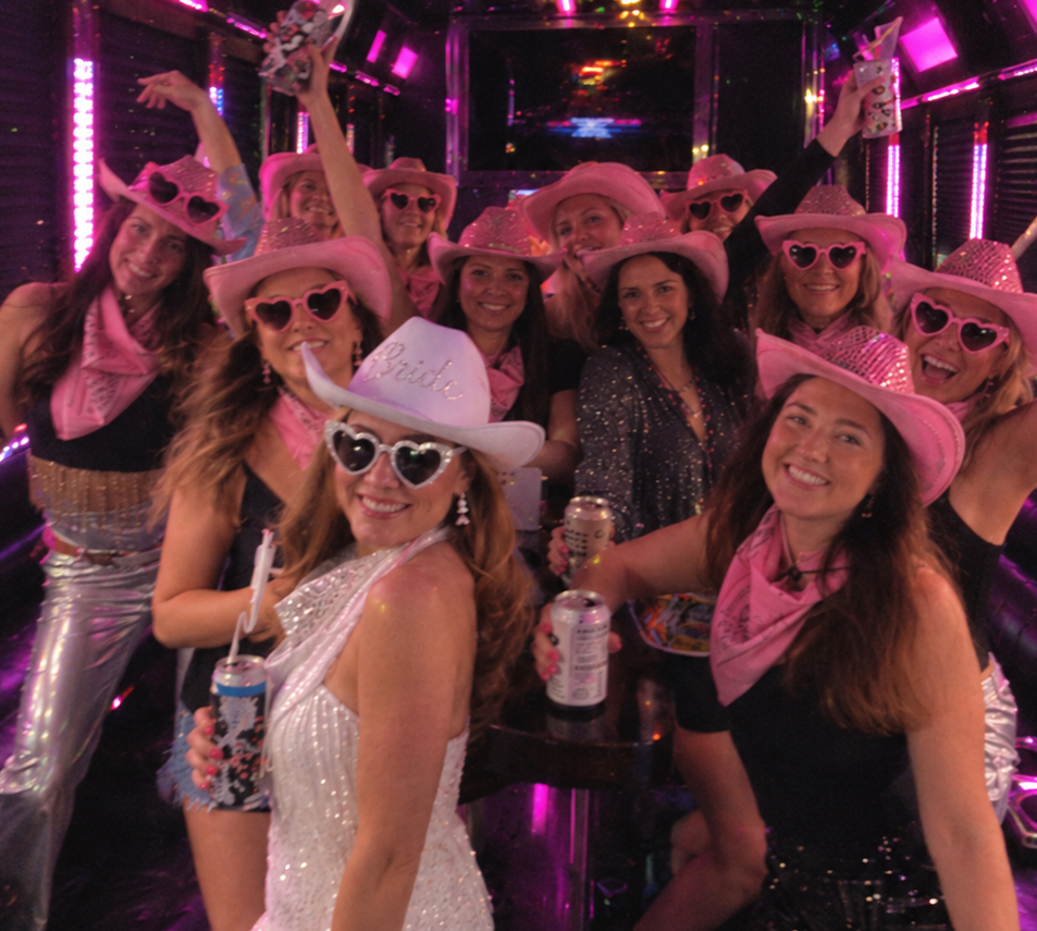 A hens crew in pink cowgirl hats and heart sunglasses on a party bus, the bride up front in a white Bride hat