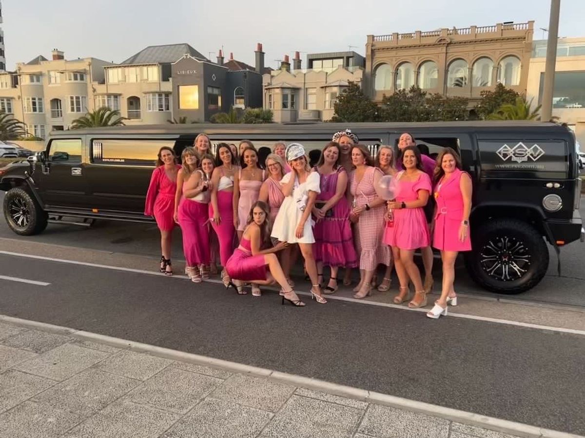 A hens group in pink standing beside a black stretch Hummer