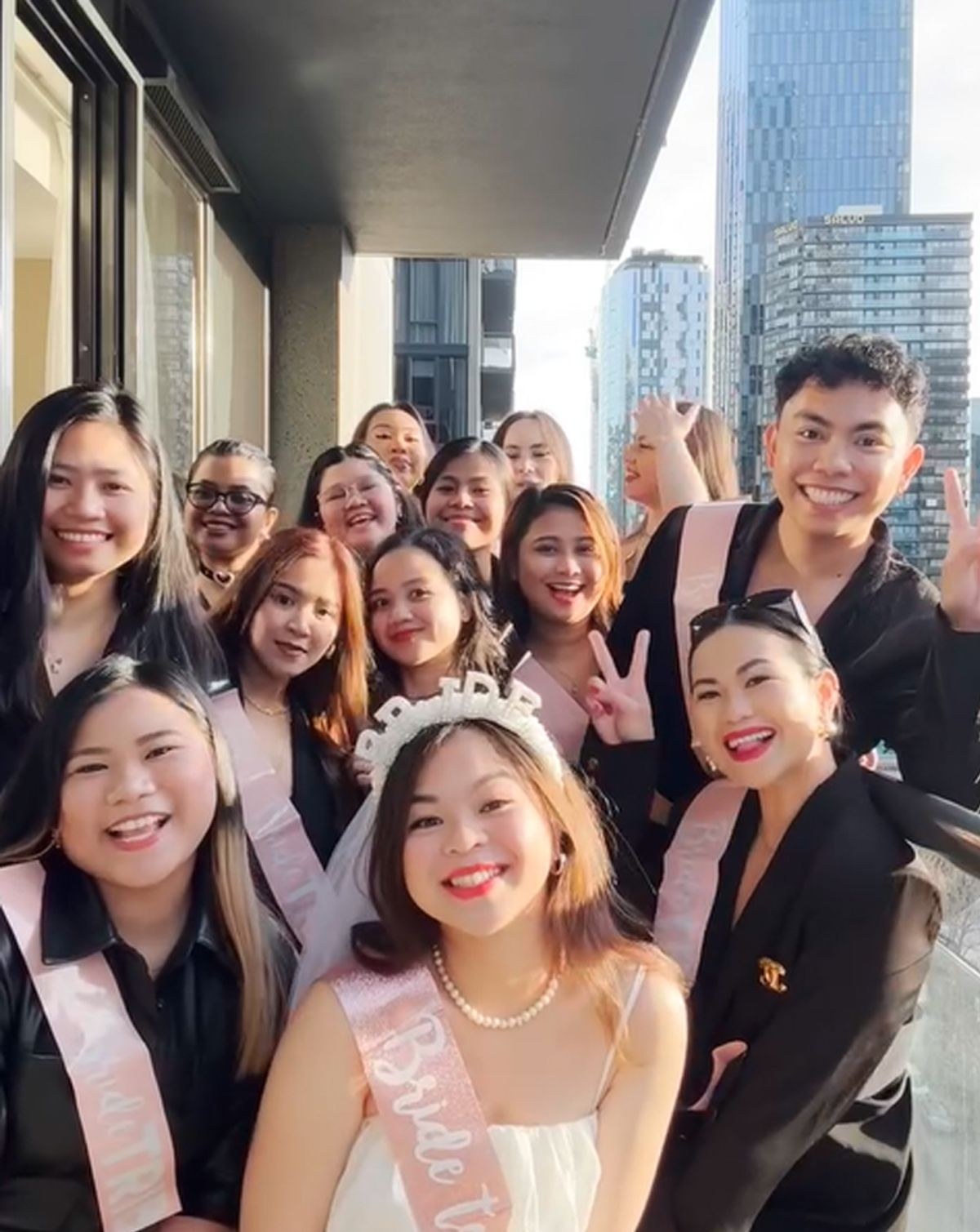 A hens group in sashes squeezing into a selfie with the bride in a veil