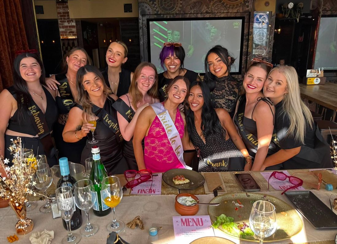 A hens group in sashes around the dinner table, the bride in a Bride to Be sash