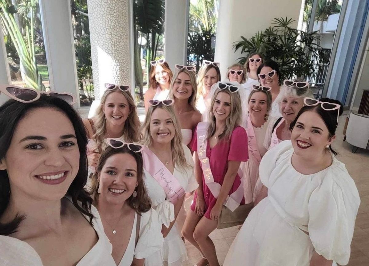 A hens group in heart-shaped sunglasses squeezing into a selfie at a bright venue