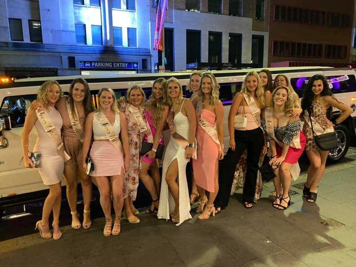 A hens group lined up in front of a white stretch limousine at night