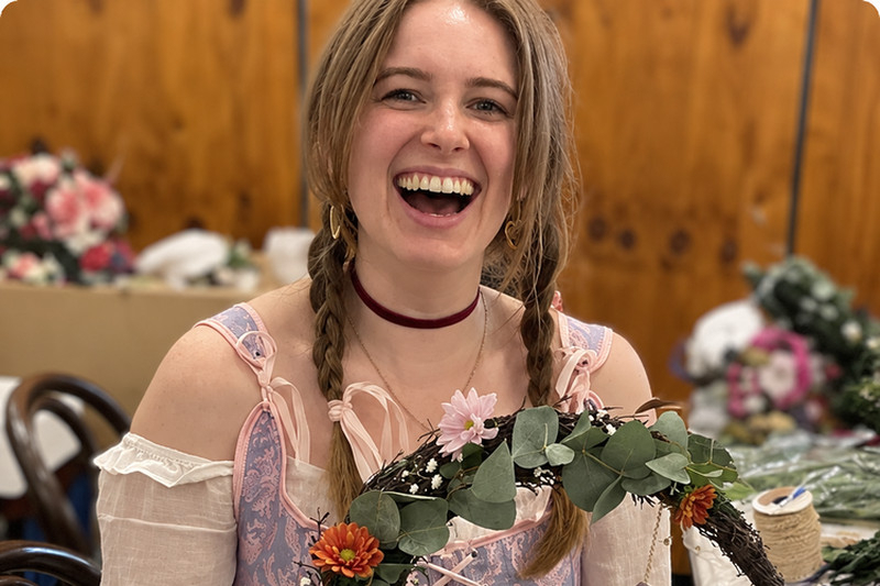 A laughing guest in plaits holding up the crescent moon wreath she made