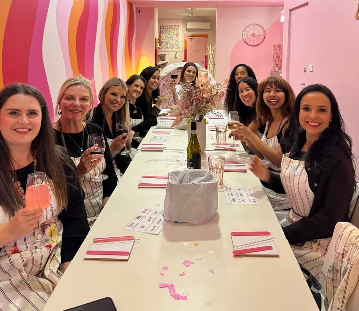 A long table of friends in aprons with glasses of wine, game sheets and pink confetti