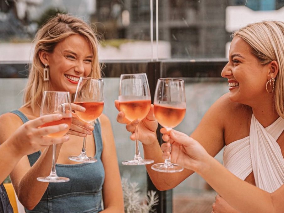 Two friends laughing and clinking glasses of rosé on a rooftop